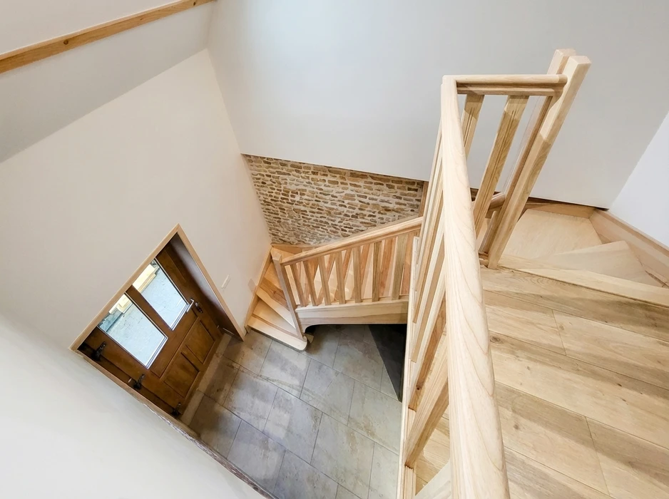 Vue en plongée d'un escalier intérieur en bois clair avec palier intermédiaire