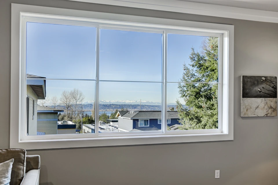 Intérieur résidentiel moderne avec grande fenêtre panoramique à trois panneaux offrant vue dégagée sur quartier pavillonnaire, montagnes enneigées et végétation
