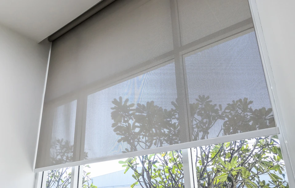 Intérieur d'habitation avec fenêtre équipée d'un store enrouleur screen partiellement baissé filtrant la lumière naturelle