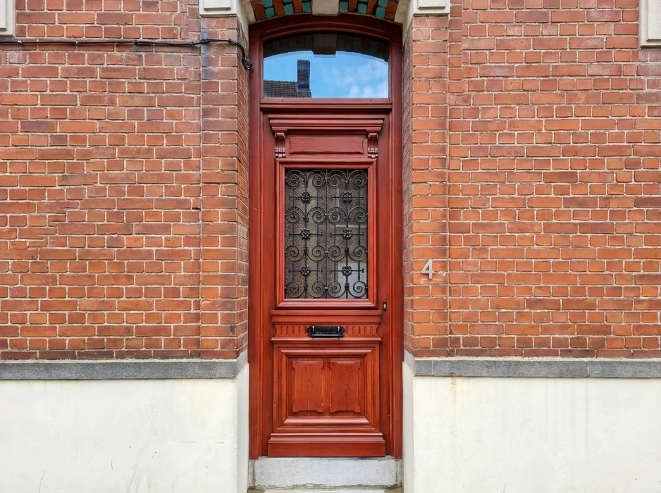 Porte d'entrée ancienne en bois massif teinte acajou, encadrée dans une façade en briques rouges
